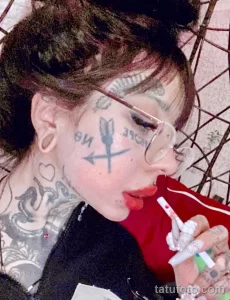 Фото тату на лице: стрела, пронзающая надпись 'love', выполненная в стиле hand-poke, минималистичный дизайн.