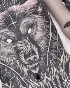 Фото тату волка на боку, выполненное в технике blackwork. Детализированный рисунок с реалистичным изображением головы волка и текстурой шерсти.