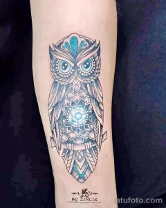 Фото татуировки совы, выполненной в стиле мандалы с использованием бирюзовых оттенков. Изображение отличается сложным геометрическим узором и высокой детализацией.