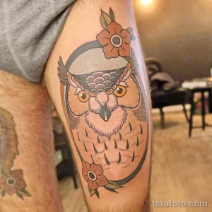 Фотография татуировки совы в стиле олдскул на ноге. Сова изображена в ярких цветах, с цветами и четкими контурами.