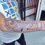 Цветная татуировка совы с большими желтыми глазами на руке. Реалистичное изображение птицы с детальной проработкой оперения.