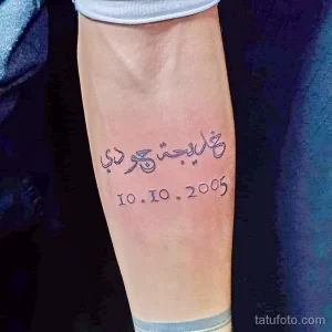 Фото тату: изящная арабская каллиграфия с датой '10.10.2005' на внутренней стороне голени. Черные чернила, четкие линии, минималистичный дизайн.