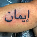 Фото тату: черная арабская надпись 'Иман' на предплечье мужчины. Простой и лаконичный рисунок татуировки.