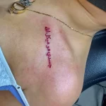 Фото тату: красная арабская надпись, расположенная под ключицей на груди. Изящный шрифт, четкие линии, минималистичный дизайн. Татуировка, несущая в себе личное послание.