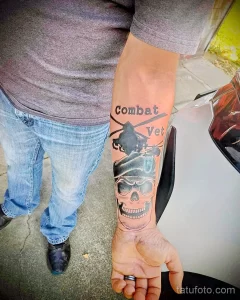 Фото татуировки на руке: череп в берете с надписью 'Combat Vet'. Черно-белый рисунок татуировки.