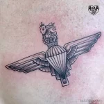 Фото тату на спине с изображением парашюта с геральдическим львом и короной. Черно-серый рисунок татуировки, выполненный в графическом стиле.