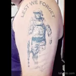 Фото татуировки на плече с изображением солдата и надписью "Lest We Forget". Черно-белый рисунок.