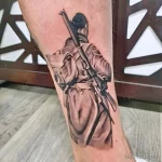 Фото тату воина в древних доспехах с копьем на ноге. Черно-белый рисунок, выполненный в реалистичной манере с акцентом на детализацию.