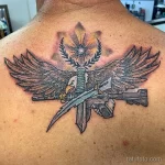 Цветная татуировка на спине с изображением орла, держащего в когтях автомат, на фоне звезды и лавровых веток.