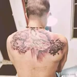 Фото тату на спине с изображением ангела, вертолета и надписи "Felipe Dylan". Татуировка выполнена в черно-серых тонах и символизирует защиту и память.