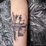 Фото тату: черно-белая татуировка на руке с изображением двух солдат, смотрящих на крест, символизирующая память и скорбь.