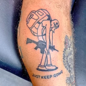 Фото тату на ноге: скелет в военной форме с винтовкой и надписью "Just Keep Going". Черно-белый рисунок татуировки в минималистичном стиле.