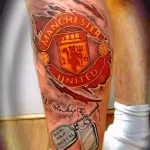 Фото тату на ноге: эмблема футбольного клуба Manchester United, автограф и изображение жетона. Цветная татуировка.