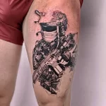 Фото тату: детализированный рисунок солдата в военной форме с автоматом и гранатами на бедре. Реалистичная татуировка в черно-серых тонах.