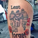 Фото татуировки на бедре с изображением солдат и надписью "Lest We Forget" (Дабы не забыть), выполненной в черно-серых тонах.