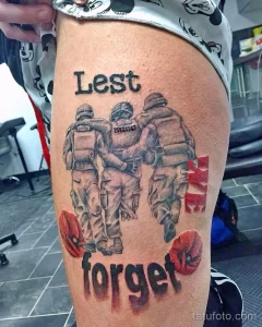 Фото татуировки на бедре с изображением солдат и надписью "Lest We Forget" (Дабы не забыть), выполненной в черно-серых тонах.