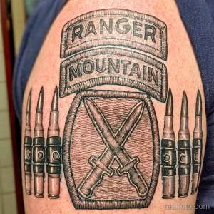 Фото татуировки на плече с изображением надписи 'Ranger Mountain' и патронов. Классический милитари стиль, четкие линии.