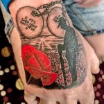 Фото тату на руке: реалистичное изображение солдатского жетона с именем и мака, символизирующего память и уважение, выполненное в черно-серых и красных тонах.