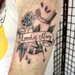 Фото тату на предплечье: черная роза с надписью 'Bloody Mary' в стиле олд скул. Детализированный рисунок татуировки с капельками.