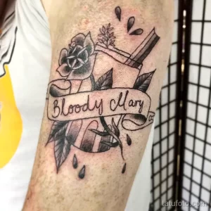 Фото тату на предплечье: черная роза с надписью 'Bloody Mary' в стиле олд скул. Детализированный рисунок татуировки с капельками.