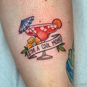 Фото тату яркого коктейля с зонтиком, фруктами и надписью "I'm a cool mom", выполненное на ноге.