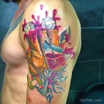 Фото тату на плече: красочный рисунок коктейля, из которого вылетают брызги. Татуировка выполнена в стиле акварель.