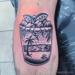 Фото черно-белой татуировки на предплечье: коктейль в бокале с пальмами, облаками и молниями. Стиль графика.