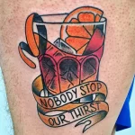 Яркое цветное фото тату с изображением коктейля в бокале и надписью "Nobody Stop Our Thirst". Татуировка выполнена в стиле олдскул.