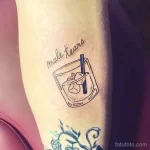 Фото тату на предплечье: стакан с коктейлем и надписью "male tears". Минималистичный стиль и тонкие линии.