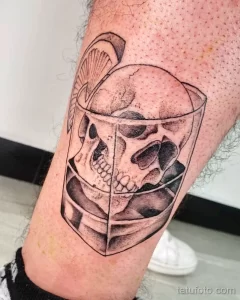 Фото тату на ноге: череп в бокале, выполненный в технике blackwork. Контрастный и выразительный рисунок татуировки.