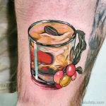 Фото тату на руке с изображением чашки кофе с кофейными зернами и листиком. Реалистичный рисунок татуировки в коричневых тонах.