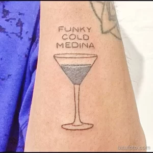 Фото тату: минималистичный рисунок бокала для мартини с надписью 'FUNKY COLD MEDINA' на предплечье. Черно-серая татуировка, выполненная тонкими линиями.