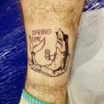 Фото тату лисы, отдыхающей в гамаке с коктейлем, с надписью 'SPRING TIME'. Черно-белый рисунок татуировки на ноге.