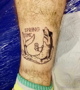 Фото тату лисы, отдыхающей в гамаке с коктейлем, с надписью 'SPRING TIME'. Черно-белый рисунок татуировки на ноге.