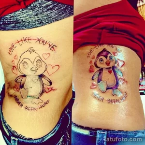 Фото тату пингвина на боку с надписью "Love like you've never been hurt". Яркий, красочный рисунок в акварельном стиле с сердечками.