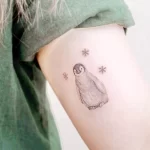 Фото тату пингвина и снежинок на бедре. Изображение выполнено в технике дотворк и имеет нежный, воздушный вид.