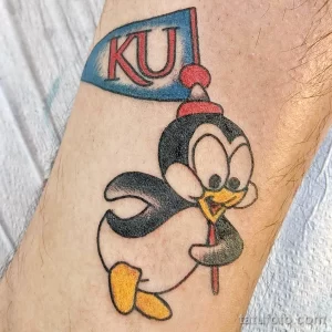 Фото тату пингвина в стиле old school с флагом и надписью 'KU'. Яркий и красочный рисунок с четкими контурами.