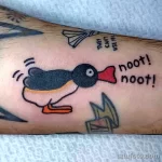 Фото яркой татуировки пингвина в стиле мультфильма с надписью "noot! noot!". Веселый рисунок татуировки на руке.