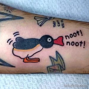 Фото яркой татуировки пингвина в стиле мультфильма с надписью "noot! noot!". Веселый рисунок татуировки на руке.