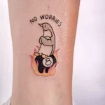 Фото тату пингвина с надписью "No Worries" и бильярдным шаром 8. Яркий дизайн, позитивный посыл, оригинальный рисунок.