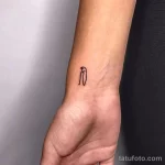 Фото минималистичной татуировки с изображением контура головы пингвина на запястье руки.