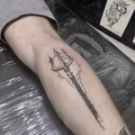 Фото тату: простой, но эффектный рисунок трезубца Посейдона в технике blackwork на икре, лаконичный дизайн.