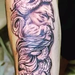 Фото тату в стиле Blackwork на руке. Изображение лица с волнистыми линиями и узорами. Черно-белая татуировка с акцентом на детали.