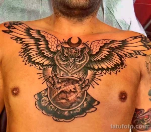 Фото тату совы на груди в стиле blackwork. Изображение включает луну, глобус и сложные узоры, выполненные черными чернилами.