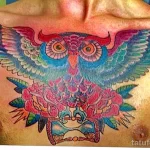 Фото красочной татуировки совы с черепом, окруженного розами на груди. Рисунок выполнен в ярких цветах, сочетающих синий, розовый и красный.