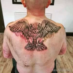 Большая черно-серая татуировка совы с расправленными крыльями на спине мужчины. Детализированный рисунок с акцентом на перья и когти.