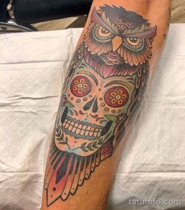 Фото тату на руке: яркая сова, стилизованная под череп в стиле Day of the Dead, с цветами и узорами. Оригинальный и красочный рисунок татуировки.