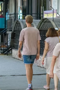 Фото тату на руке мужчины, идущего по улице. Виден небольшой рисунок на предплечье. Городской пейзаж и повседневная жизнь.