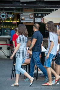 Фото тату на руке мужчины, идущего по улице. Виден фрагмент татуировки с детальной проработкой. Городской пейзаж и повседневная жизнь.