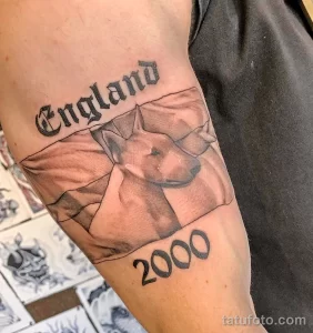 Фото тату: на руке изображен реалистичный портрет носорога с надписью "England" и годом "2000".